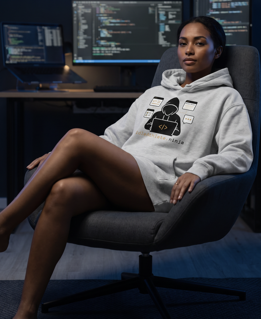 A woman wearing an idleAthlete hoodie in a chair at a coding workstation.